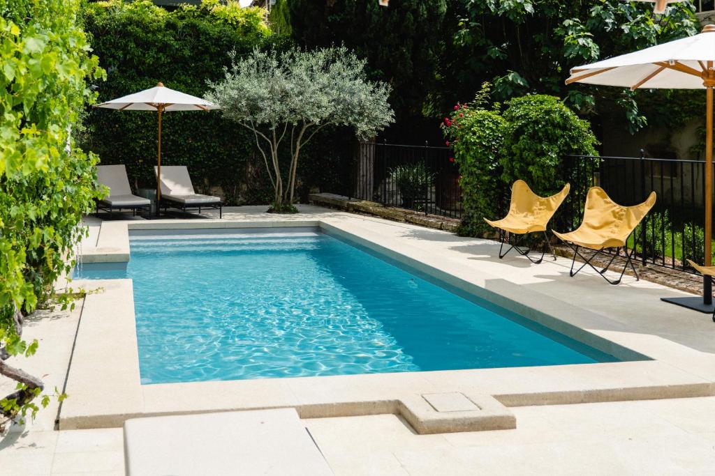 a swimming pool with chairs and umbrellas in a backyard at Le Moulin, Lourmarin, a Beaumier Hotel in Lourmarin