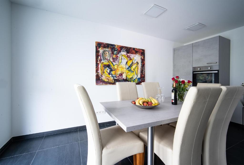 - une table à manger avec des chaises blanches et une corbeille de fruits dans l'établissement Blauer Stein Apartments WH1, à Pulheim