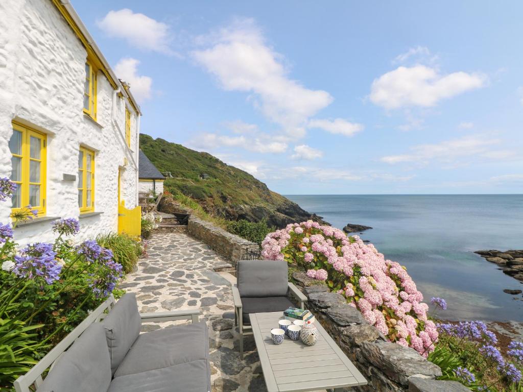 a house with a table and flowers next to the ocean at Kerbenetty Harbour Cottage in Portloe