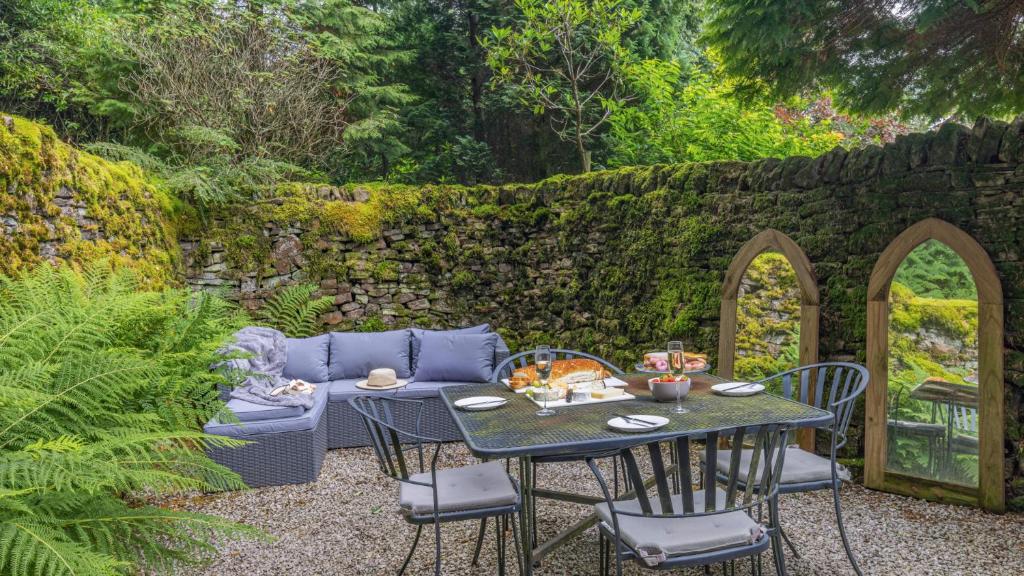 a patio with a table and chairs and a stone wall at Kestrel Cottage in Chinley