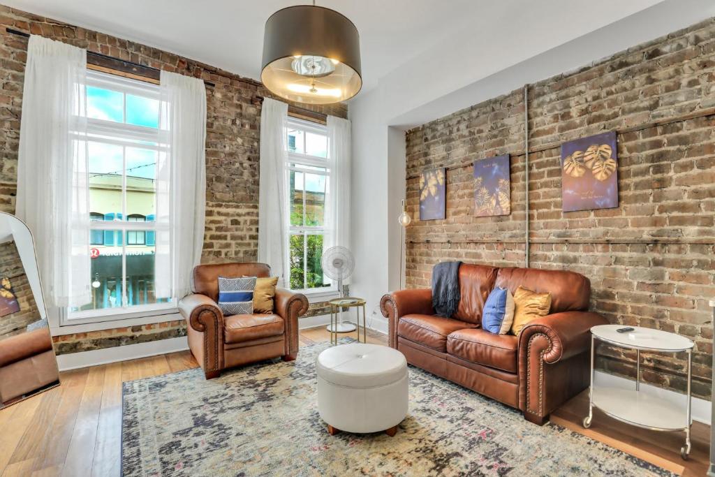 a living room with leather furniture and a brick wall at Lush Savannah Loft - Near Plant Riverside District in Savannah