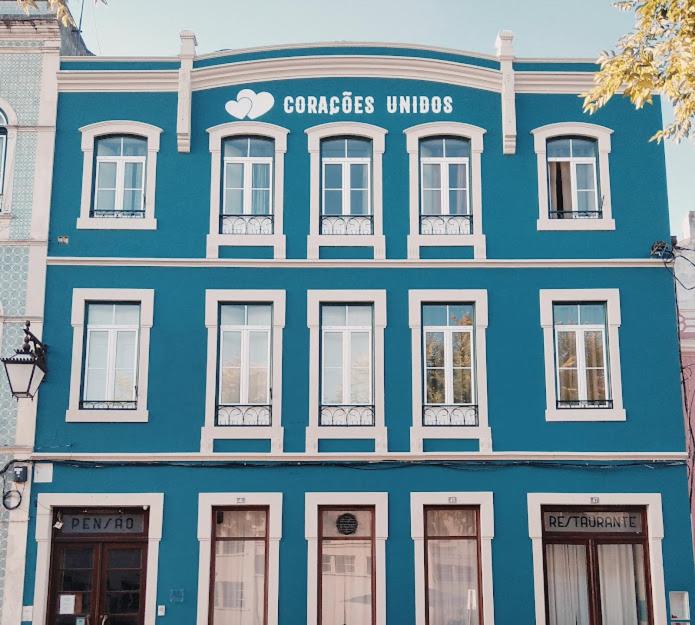 a blue building with white windows on a street at Corações Unidos "A Pensão" in Alcobaça