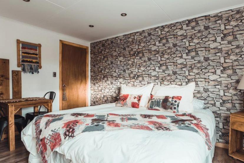 a bedroom with a bed with a stone wall at Hostal Lago Cóndor in Puerto Natales