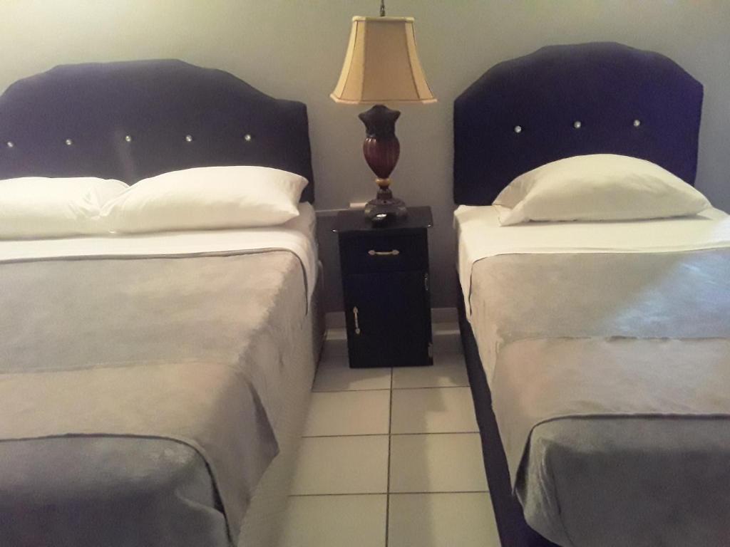 1 dormitorio con 2 camas y mesita de noche con lámpara en Derick's Inn en Piarco