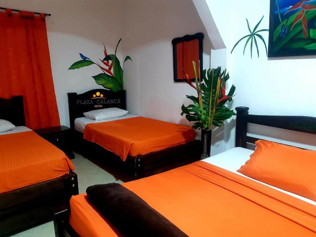 a room with two beds with orange sheets and a plant at Hotel Plaza Calarcá in Calarcá