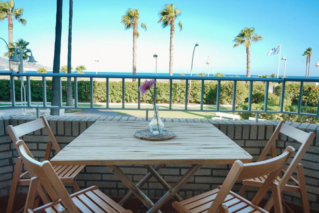 a wooden table and chairs on a deck with palm trees at Bonito apartamento en primera línea de playa in Motril