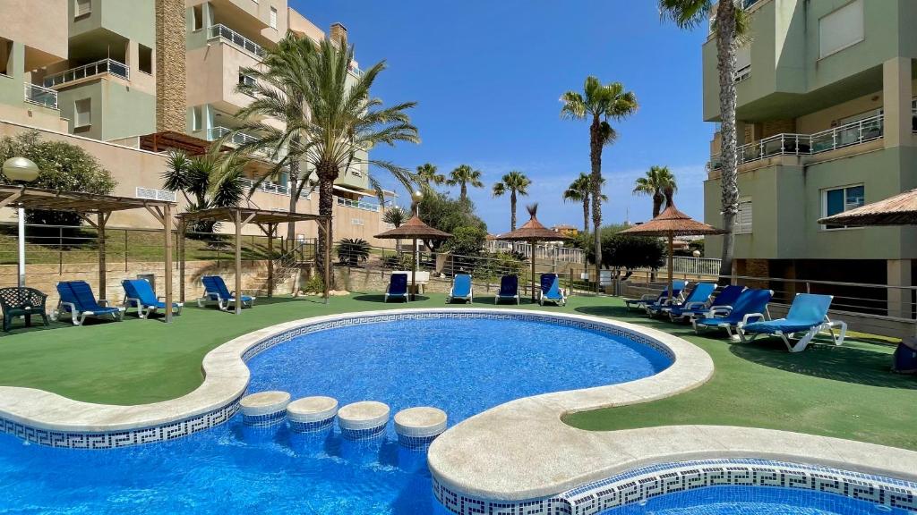 Una piscina en un resort con sillas azules y palmeras. en Cala AZUL Gran Terraza con BBQ, en Cabo de Palos
