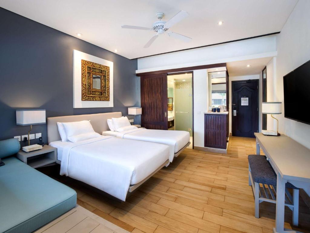 a hotel room with two beds and a desk at Novotel Bali Benoa in Nusa Dua