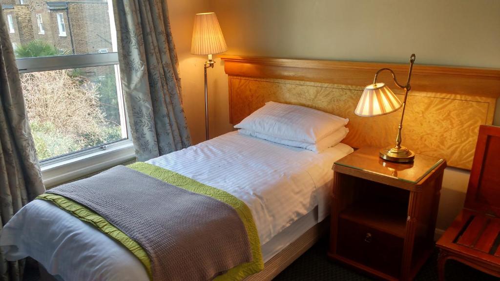 een slaapkamer met een bed met een lamp en een raam bij Hotel Sergul in Londen