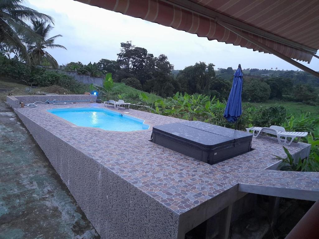 a swimming pool with an umbrella on a patio at Entre Mer et Montagne in Goyave