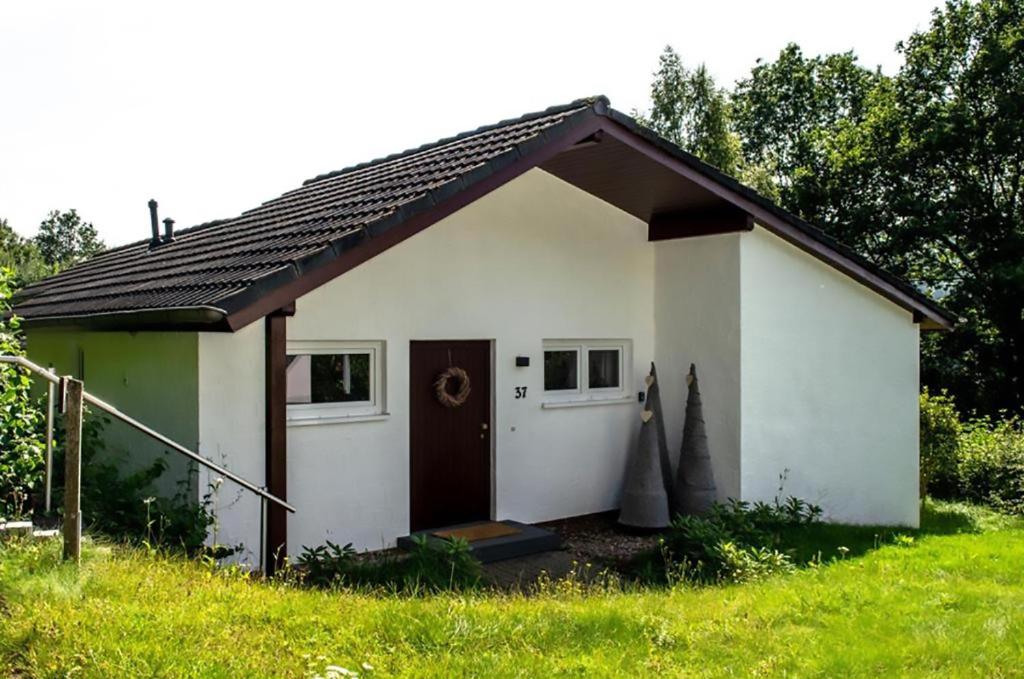 a small white house with a door in a field at Eifel Cottage Biersdorf am See in Biersdorf