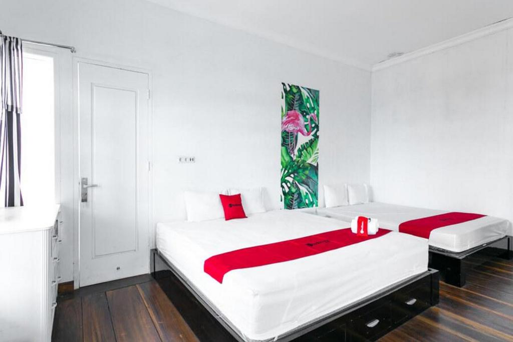 a white bedroom with two beds with red pillows at RedDoorz near Grojogan Sewu Tawangmangu in Karanganyar
