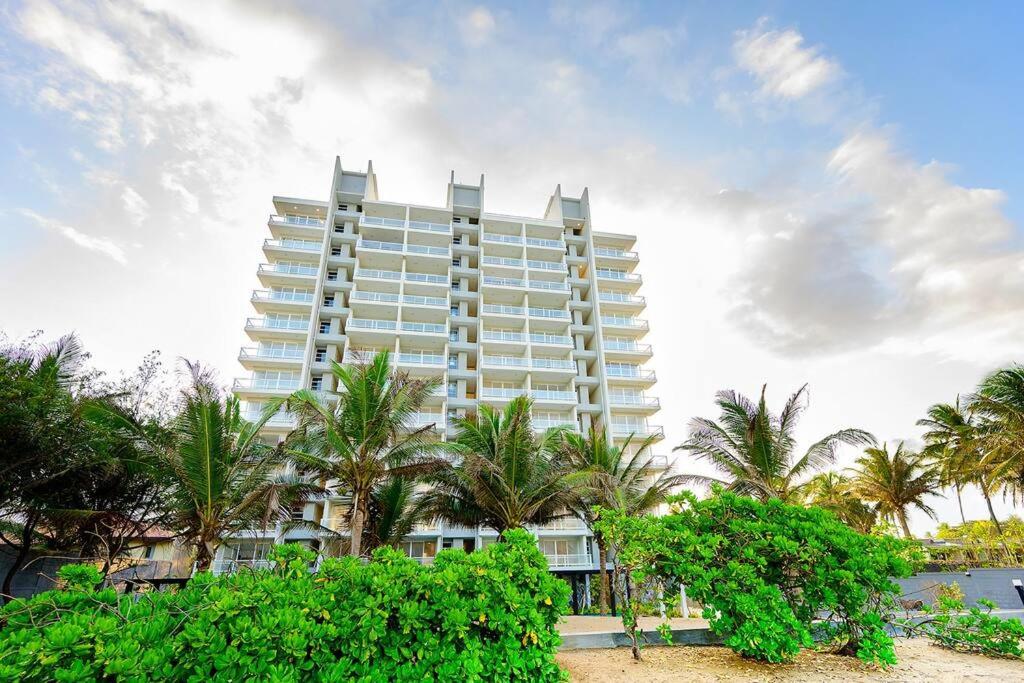a large white building with palm trees in front of it at MaSa Beach Front Apartment Uswetakeiyawa in Ja-Ela
