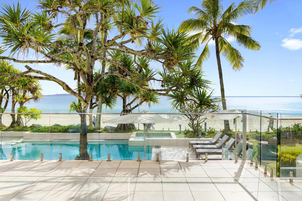 a resort pool with palm trees and the ocean at Fairshore Apartment 12, Noosa Heads in Noosa Heads