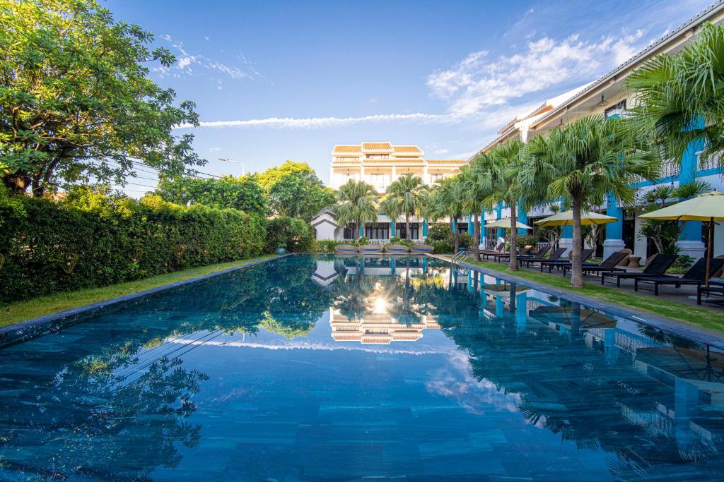 a swimming pool with palm trees and a building at Thanh Binh Riverside Hoi An in Hoi An
