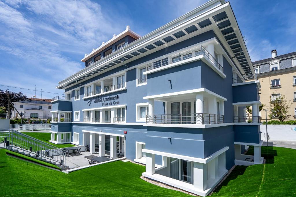 un edificio azul con un césped verde delante de él en abba Apartments Playa de Gros San Sebastián, en San Sebastián