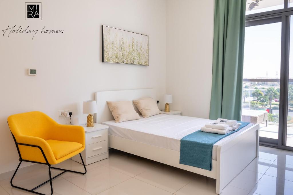 a white bedroom with a bed and a yellow chair at Mira Holiday Homes - Spacious Studio with Balcony - Free Wifi in Dubai