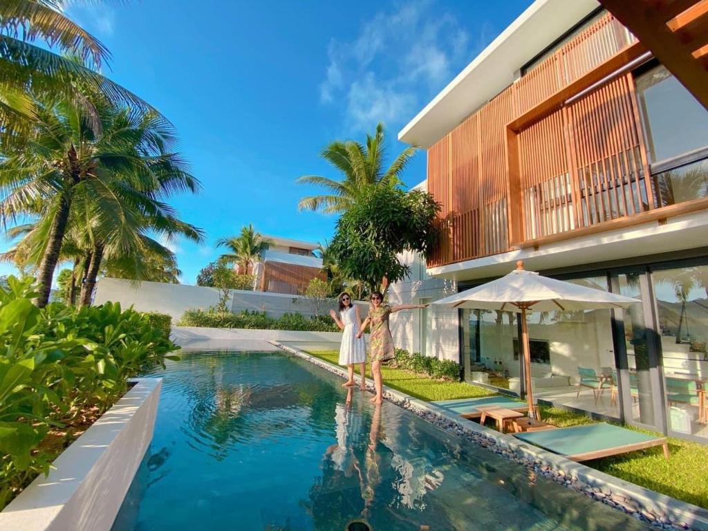 two people standing by a swimming pool in front of a house at Phoenix Pool Villa Phu Quoc in Phu Quoc