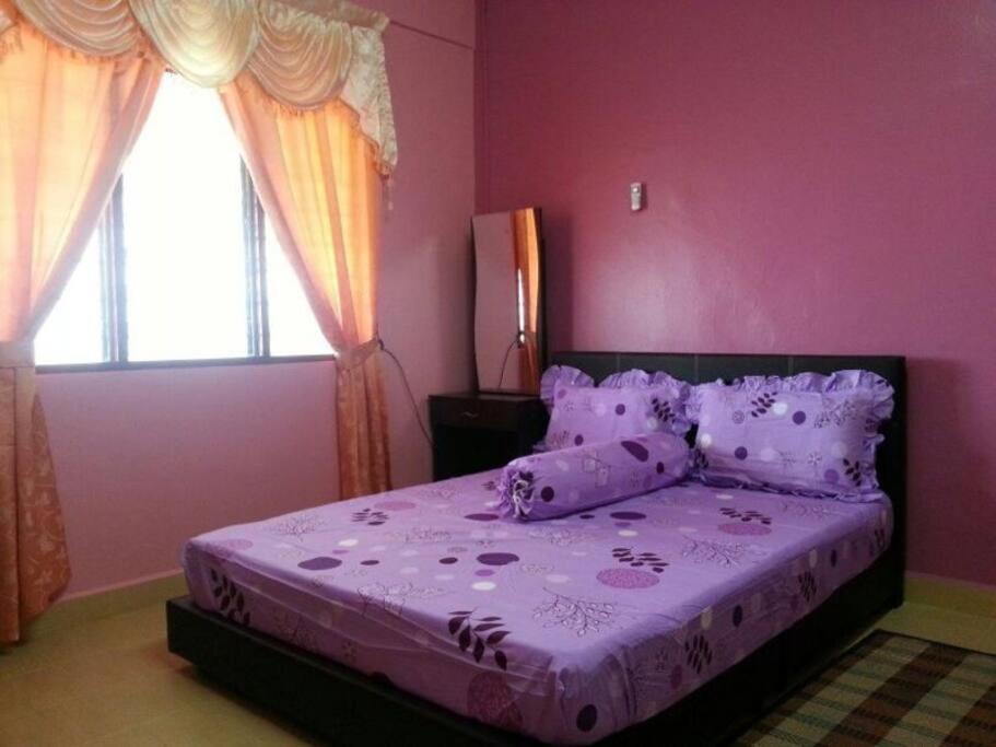 a pink bedroom with a bed with purple sheets and pillows at D'FIEZA HOMESTAY KEMAMAN in Cukai