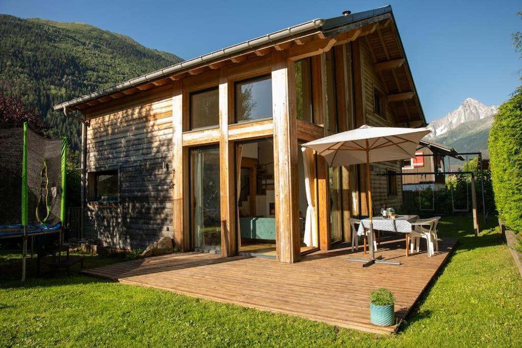 ein Haus mit einer Holzterrasse mit einem Tisch und einem Sonnenschirm in der Unterkunft Family Chalet 3 Bedrooms + Sauna + Mountain Views in Les Houches