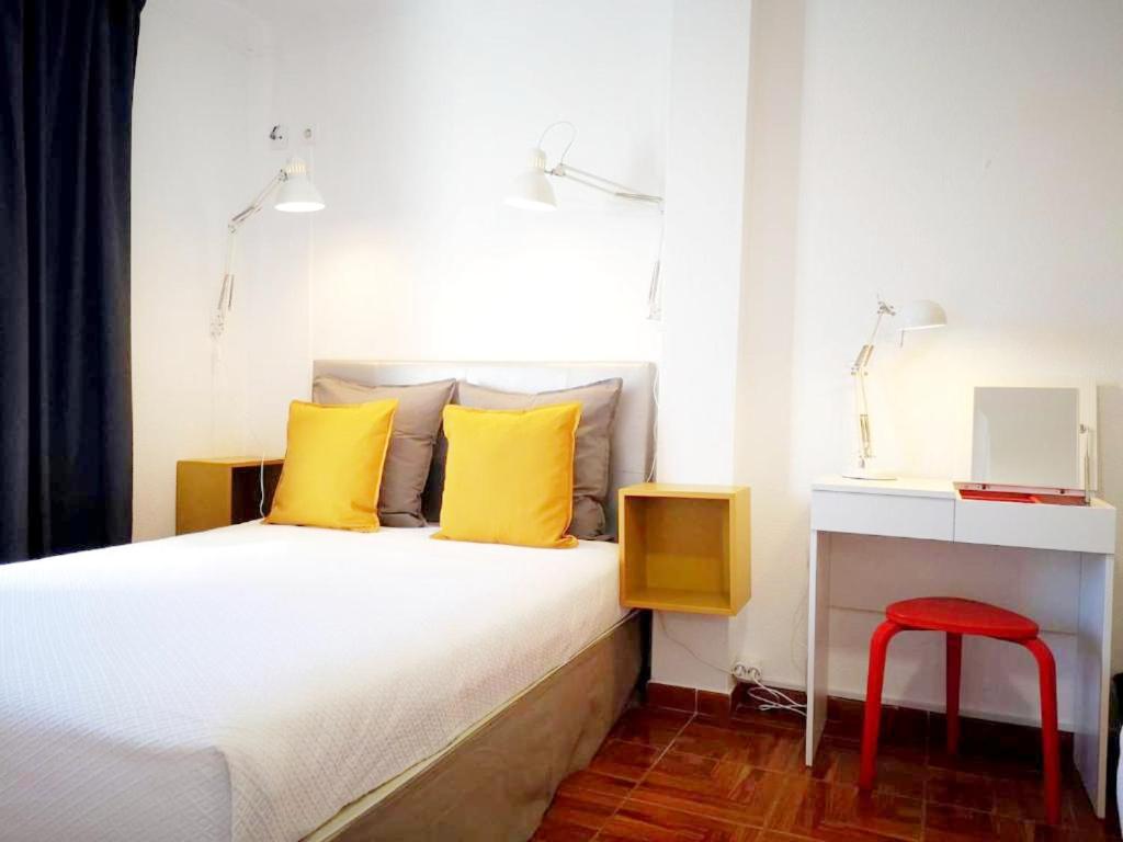a bedroom with a bed with yellow pillows and a red stool at The Bulldog Inn - Duna Parque Group in Vila Nova de Milfontes