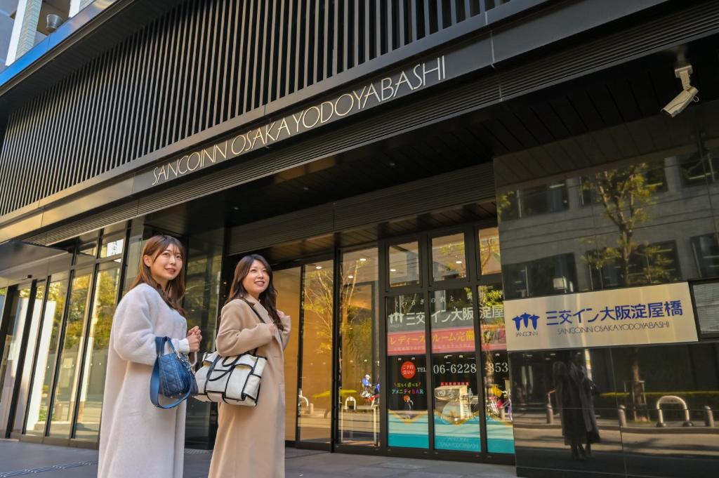 zwei Frauen stehen vor einem Gebäude in der Unterkunft Sanco Inn Osaka Yodoyabashi in Osaka