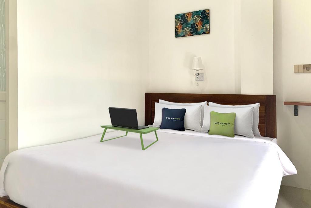 a bedroom with a large white bed with a laptop on it at Urbanview Hotel SLIP Pringsewu by RedDoorz in Margakaya