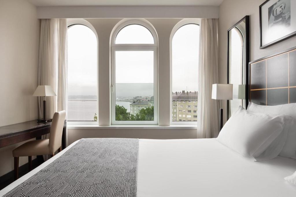 a bedroom with a bed and a desk and windows at Eurostars Ciudad de La Coruña in A Coruña