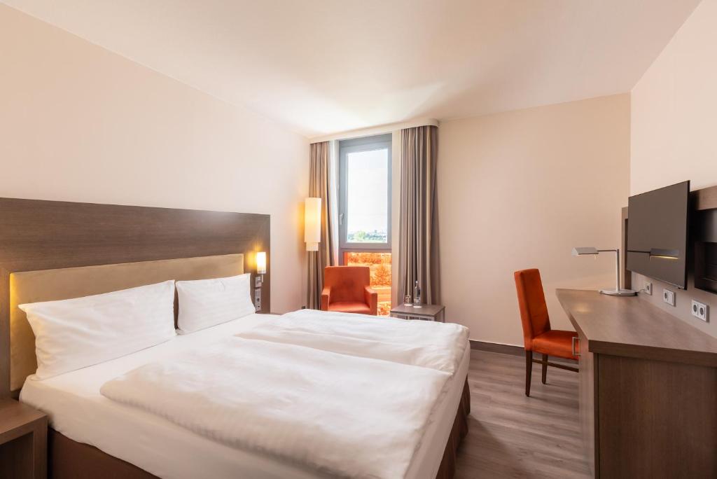 um quarto de hotel com uma grande cama branca e uma secretária em IntercityHotel Berlin Airport Area North em Schönefeld