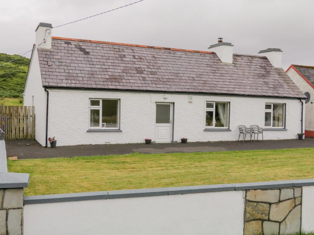 a white house with chairs in the yard at Maghera Caves Cottage in Ardara