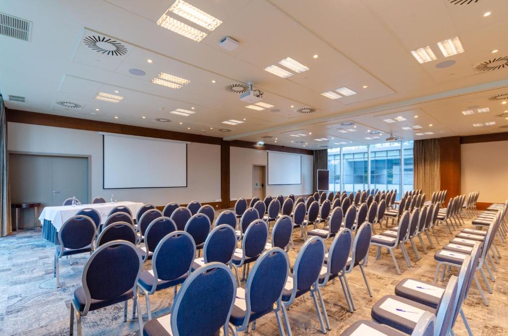 A large auditorium-style conference room with rows of chairs and two screens.
