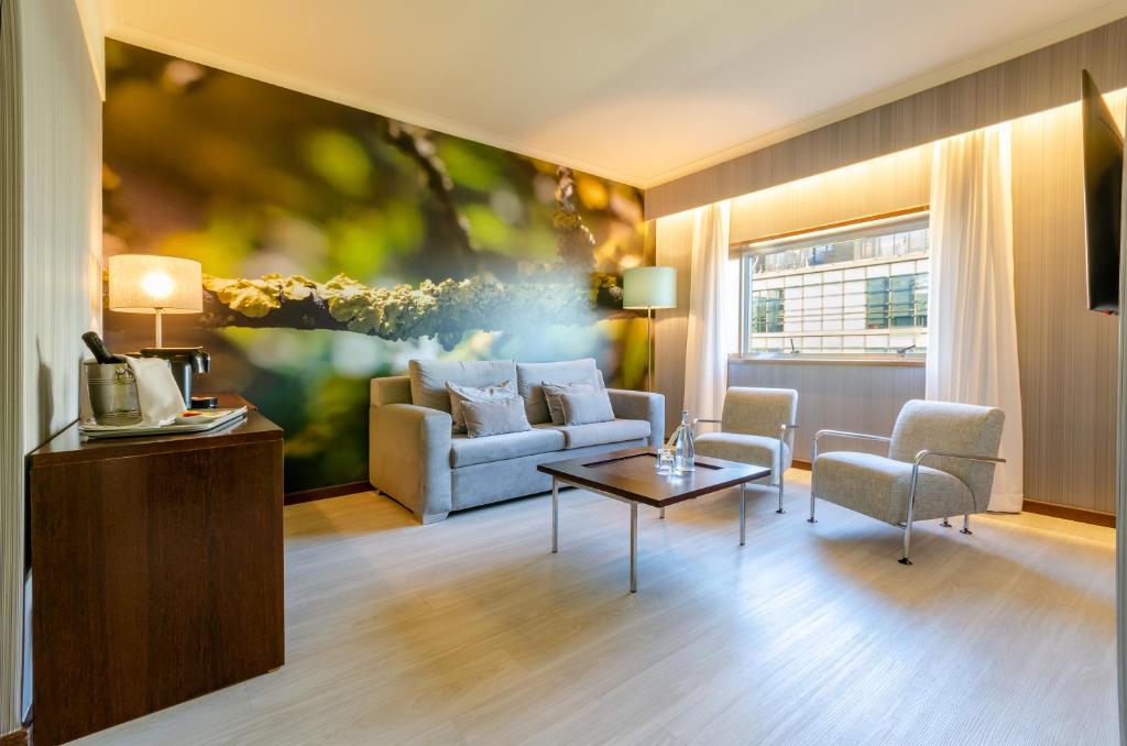 A bright lounge with a sofa, armchairs, nature mural and a street-facing window.