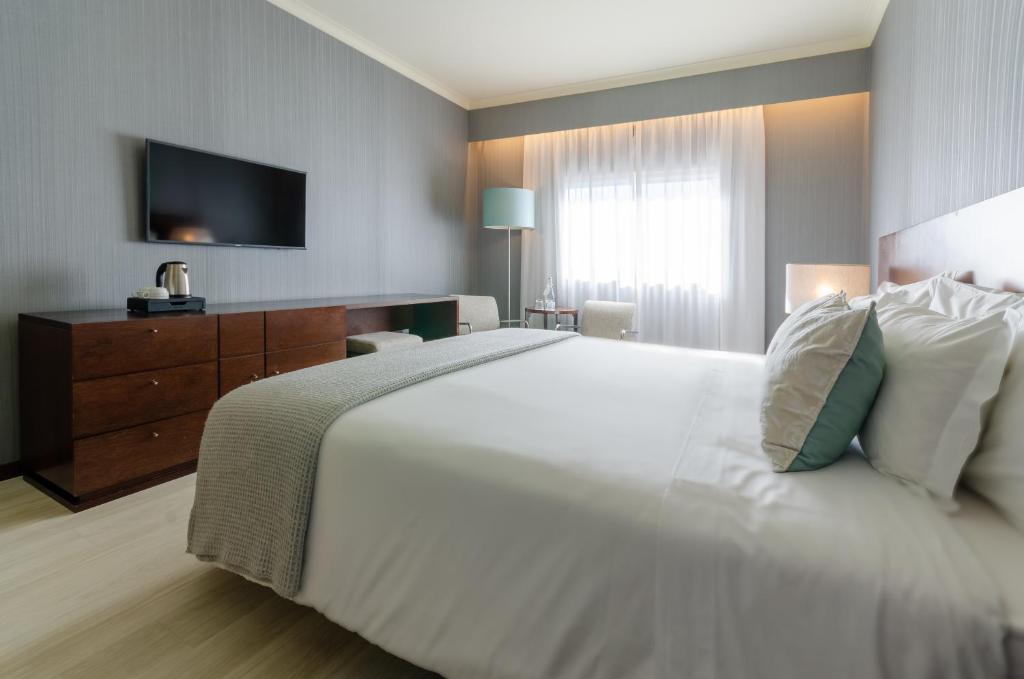 A neatly made bedroom with a large bed, dresser, television and window-side seating.