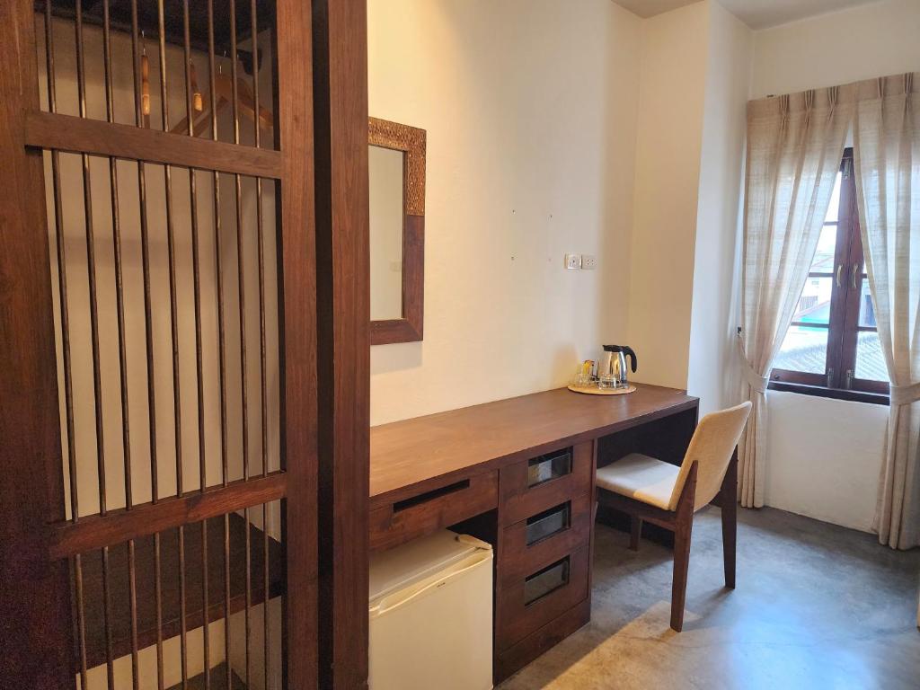 A bedroom work area with a long wooden desk, upholstered chair, kettle, and compact refrigerator.