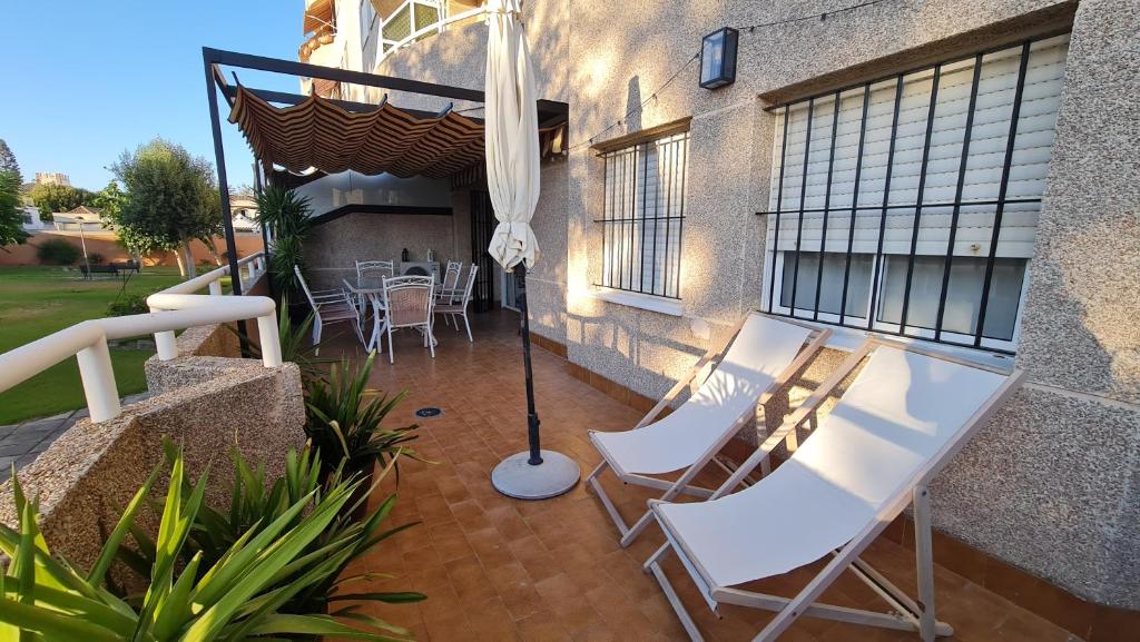 a patio with two white chairs and an umbrella at APTARTAMENTO DOÑANA RECIEN REFORMADO Parking gratis in Sanlúcar de Barrameda
