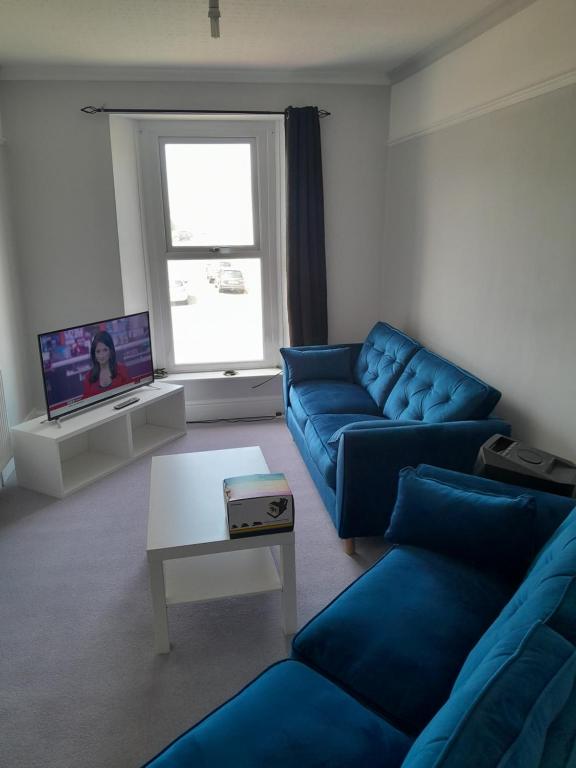 a living room with blue couches and a tv at Conveniently located, newly refurbished flat (sleeps 4) in Pembrokeshire