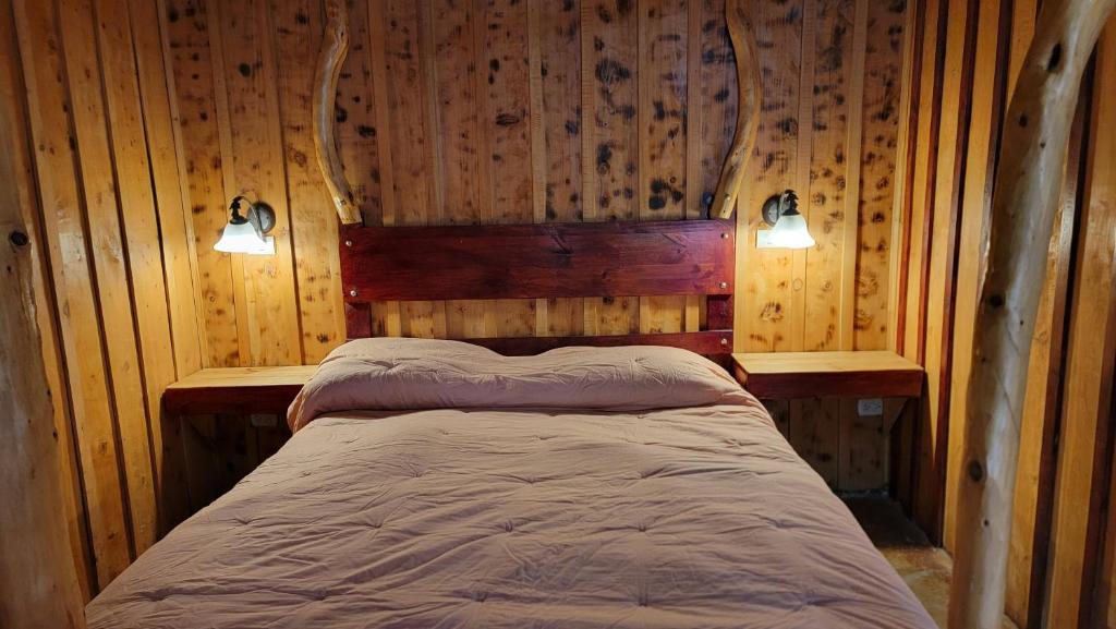 a bed in a room with wooden walls and two lights at Poas Volcano & La Paz Waterfall Cabins 