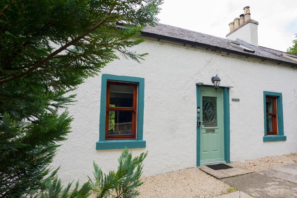 ein weißes Haus mit blauen Fenstern und einer grünen Tür in der Unterkunft Tig Cottage - a rural, quirky, pet friendly 2 bedroom cottage near Ballantrae in Ballantrae