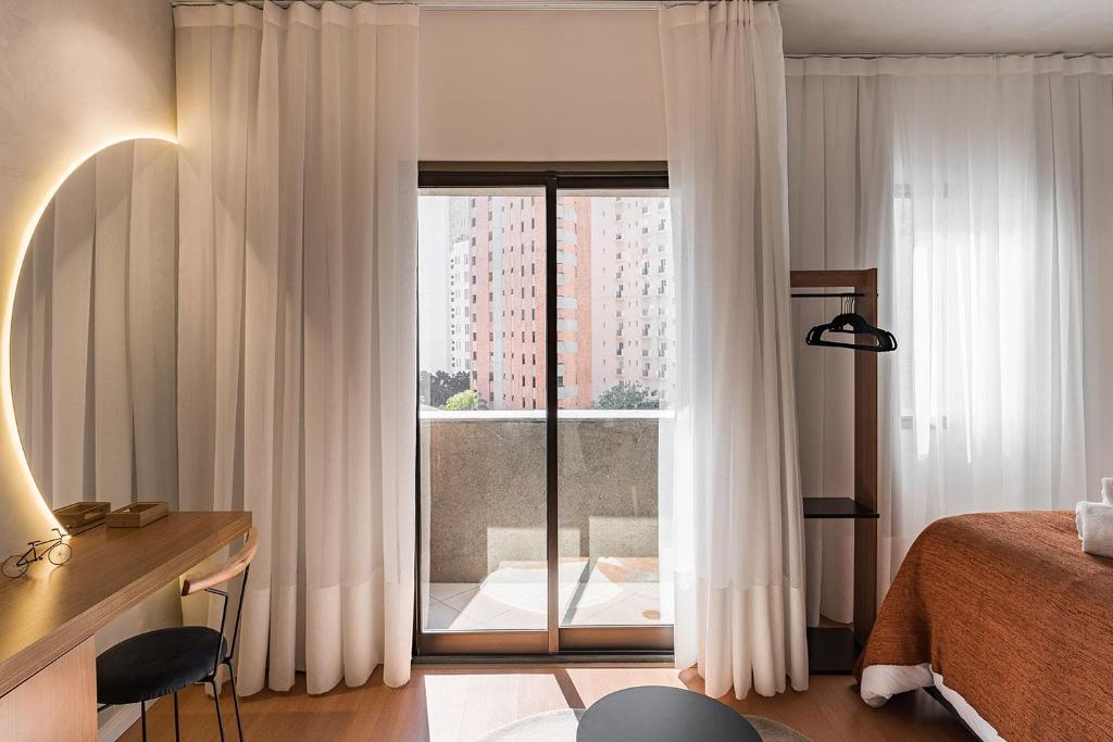 a bedroom with a bed and a glass door with a window at Cyclinn Jesuíno Arruda Itaim in São Paulo