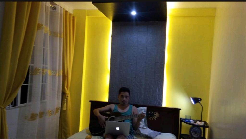 Ein Mann, der mit einer Gitarre und einem Laptop im Bett sitzt. in der Unterkunft Guest Homey in Iloilo City