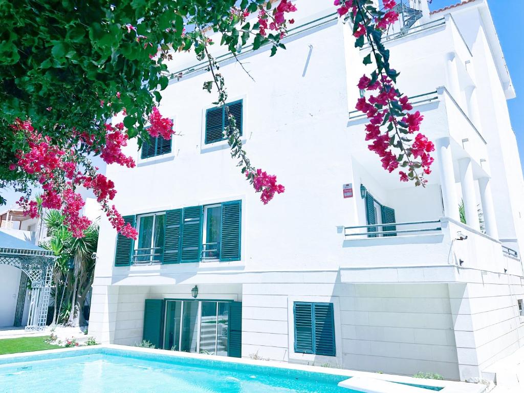 een wit gebouw met een zwembad en roze bloemen bij Yo-House in Costa da Caparica