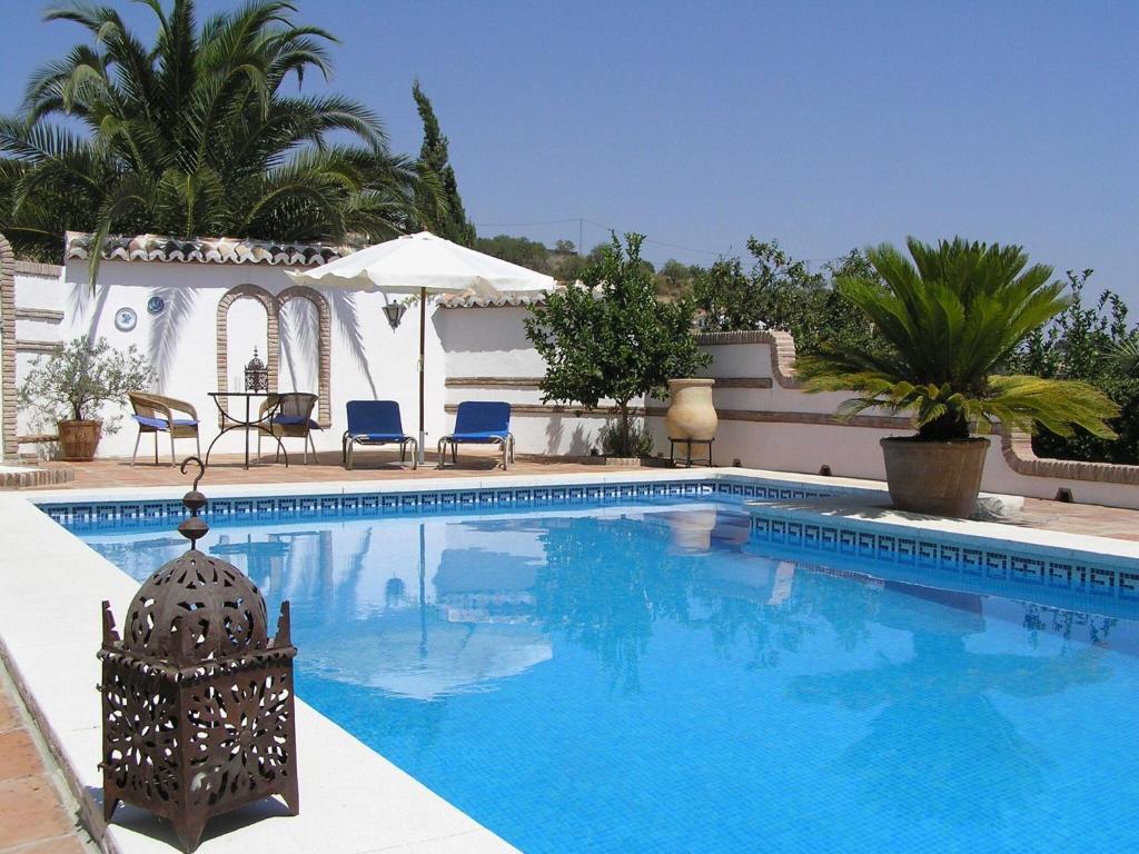 a swimming pool with chairs and a table and palm trees at Guest house in a traditional Andalusian country estate in La Joya