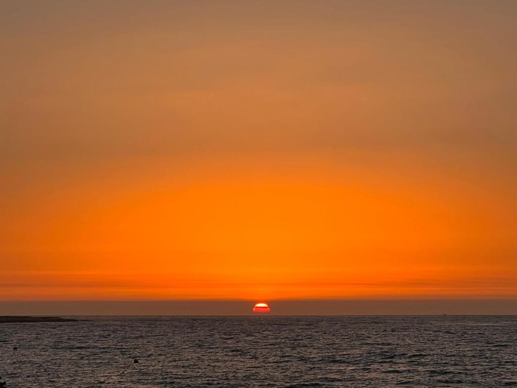 una puesta de sol naranja sobre el océano con el sol en la distancia en Forêt appartement, en Tánger