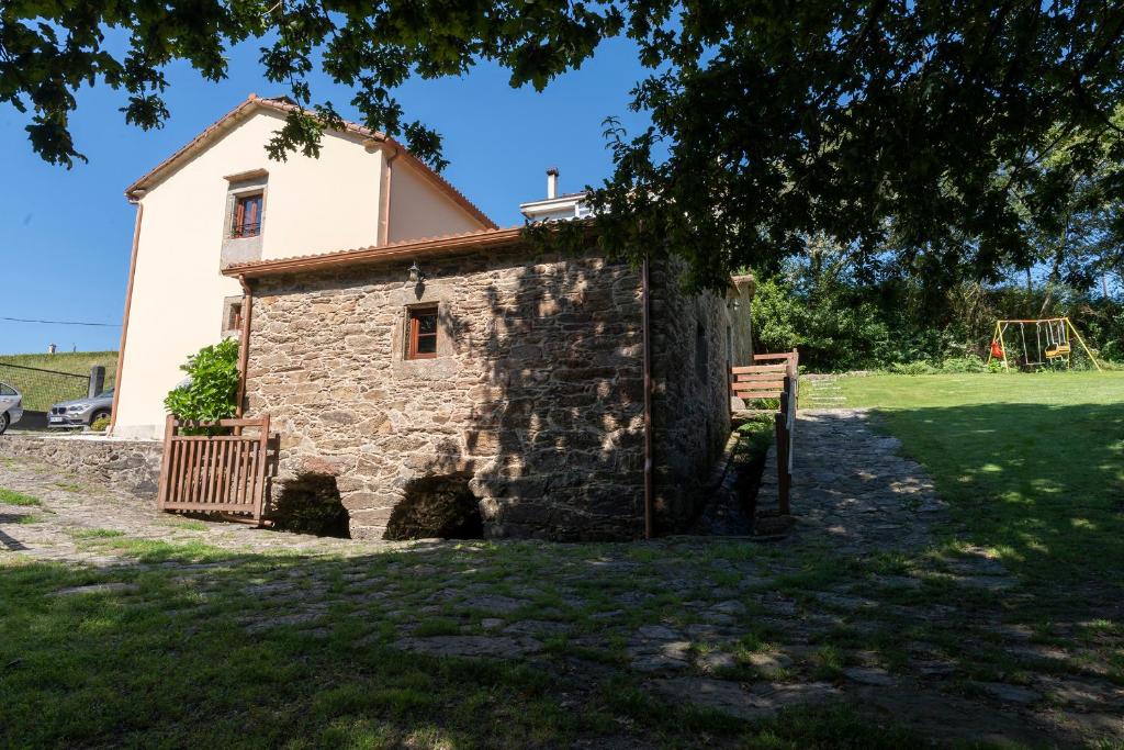 una antigua casa de piedra con un patio de recreo en el fondo en Casa rural completa Río Sarela, en Santiago de Compostela