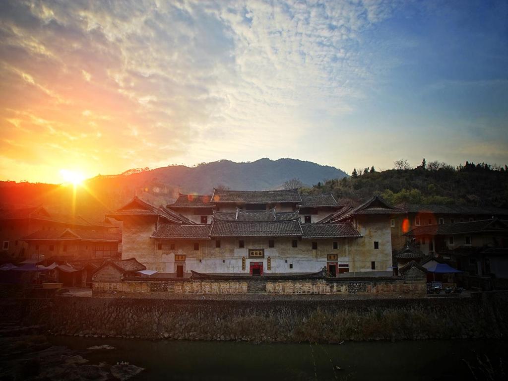 un edificio asiático con la puesta de sol en el fondo en Tulou Fuyulou Changdi Inn, en Yongding