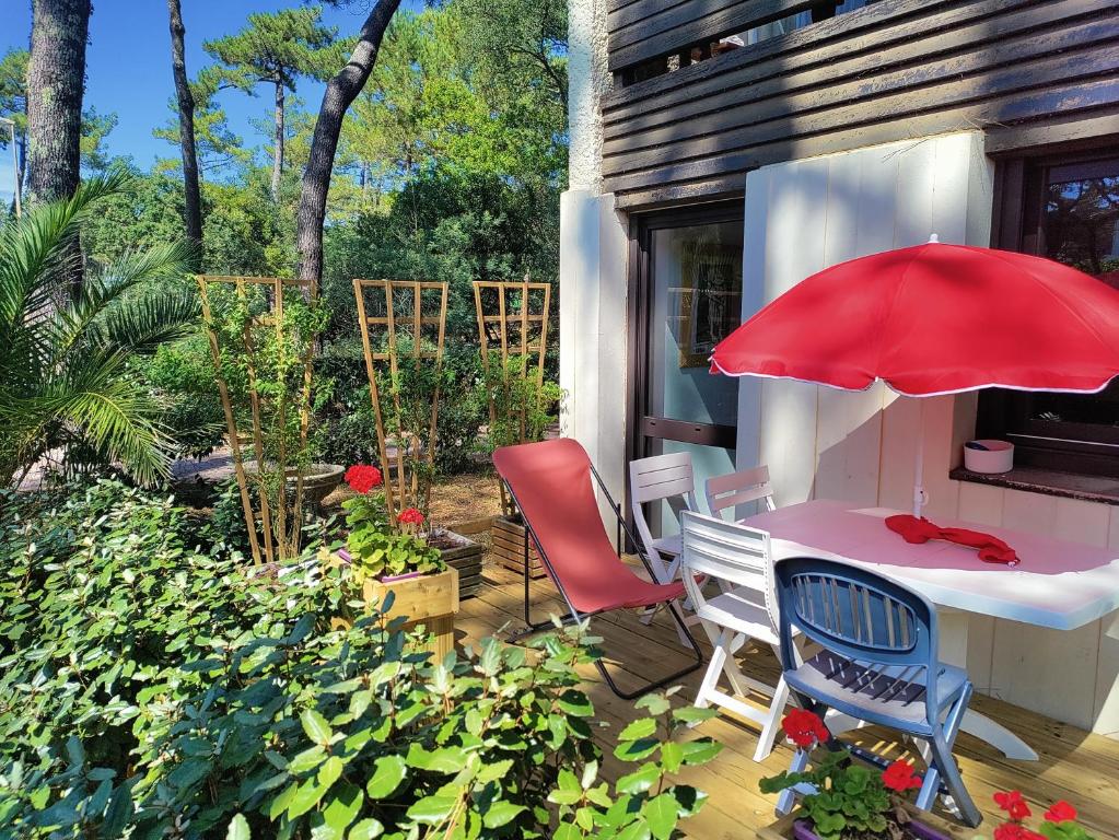 d'une terrasse avec une table, des chaises et un parasol rouge. dans l'établissement Appt Seignosse le Penon - plages commerces à pied, à Seignosse