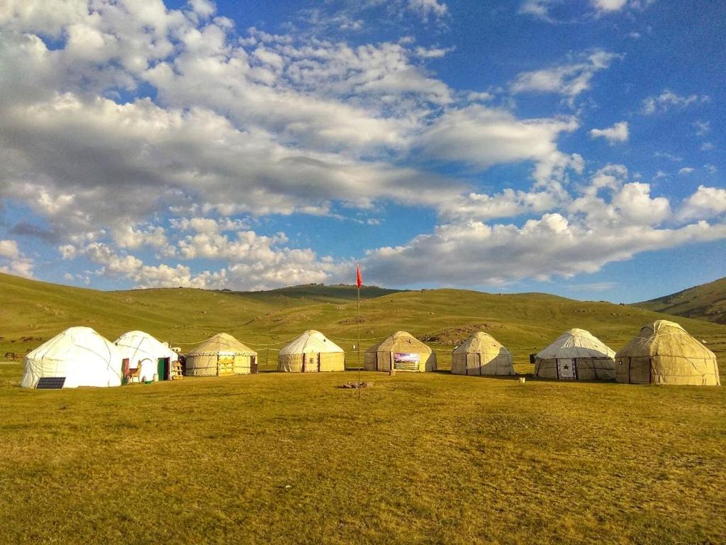 a group of domes in a field with a cloudy sky at Song Kol lake, Flex Travel yurt camp, horse riding in Song-Kul