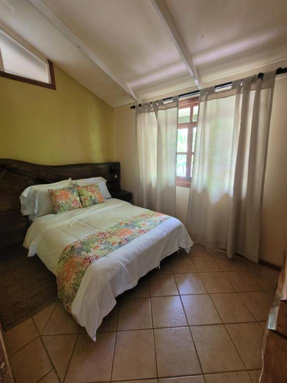 a bedroom with a bed with white sheets and a window at Cabina Rancho la Merced in Uvita