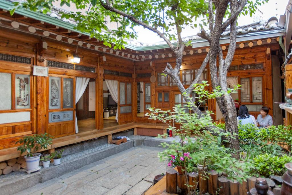 Dongmyo Hanok Sihwadang - Private Korean Style House in the City Center with a Beautiful Garden في سول: منزل خشبي أمامه شجرة