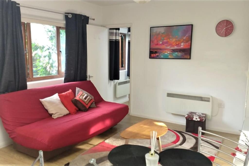 a living room with a red couch and a table at Modern Spacious Detached Cottage in Cambridge in Cherry Hinton